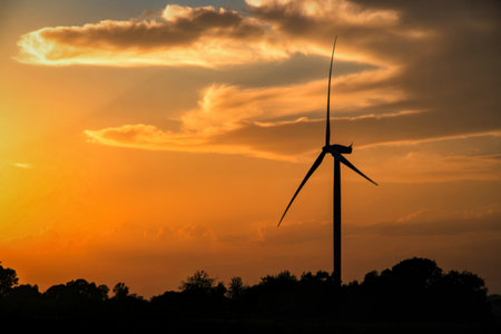 A lone wind turbine stands silhouetted against a dramatic sunset, with warm orange and yellow hues...