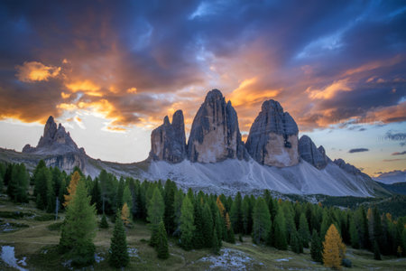 Majestic Tre Cime di Lavaredo mountains bathed in the warm glow of a vibrant sunset, with a dense forest in the foreground.の写真素材