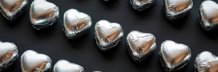 A close-up, overhead view of numerous metallic silver heart-shaped balloons arranged on a dark, textured surface.の写真素材