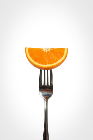 A bright, juicy orange slice is presented on a metallic fork, isolated against a clean white backdrop, suggesting a healthy snack or ingredient.の写真素材