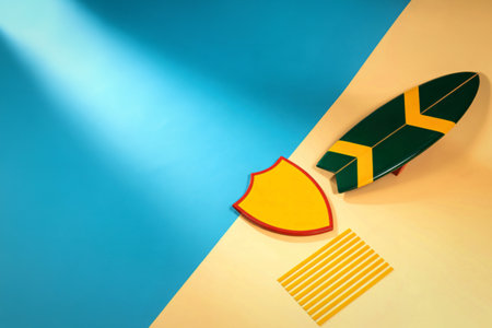 A stylized flat lay featuring a surfboard, a yellow shield shape, and a small striped mat on a split blue and tan surface.の写真素材