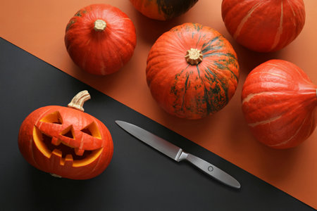 A carved jack o lantern sits next to a knife on a black surface, with several uncarved pumpkins in...