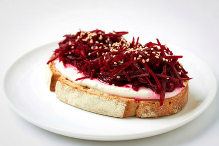 A close-up shot of a single slice of toasted bread topped with creamy white spread and shredded beetroot, sprinkled with sesame seeds.の写真素材