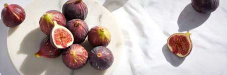 A collection of whole and halved ripe figs, showcasing their vibrant interior, bathed in natural sunlight casting shadows on a white textured surface.の写真素材