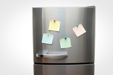 A close-up view of a sleek stainless steel refrigerator door adorned with four colorful sticky notes, attached with small pins.の写真素材
