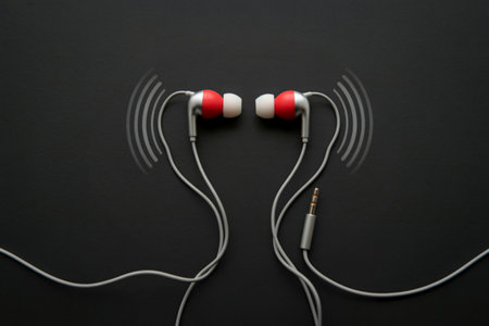 A pair of red and white earbuds are shown with stylized sound waves emanating from them against a stark black backdrop.の写真素材