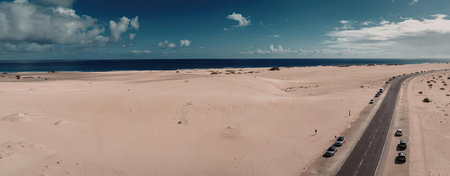 A panoramic view of a desert road that stretches towards the ocean, with a clear blue sky and...