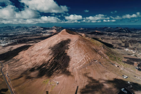 An aerial view of a large brown mountain with a blue sky and white clouds in the background.