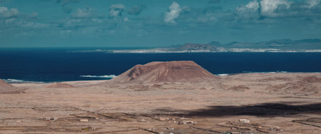 A large brown landmass near a body of water under a blue sky with clouds.