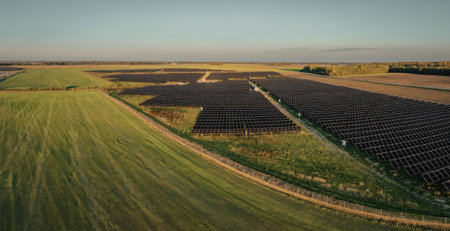 An aerial view of a large solar farm situated in a rural area with green fields and a clear sky