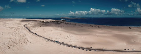 A panoramic view of a sandy beach with a fence running along it, meeting the vast ocean under a...