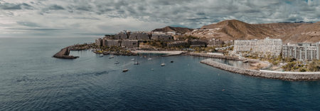 The image depicts a coastal town with a large body of water and a mountainous backdrop. The town is...