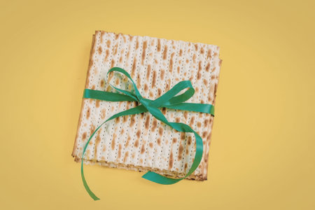 The image features a square of matzo, a traditional Jewish food, tied with a green ribbon and set...