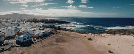 A panoramic view of a coastal town with white buildings, a sandy beach, and a vast ocean.
