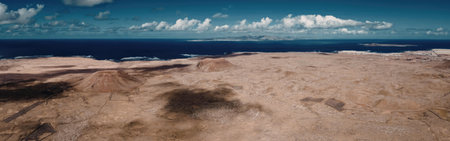 A panoramic view of a coastal landscape with a vast expanse of dry, brown terrain meeting the blue...