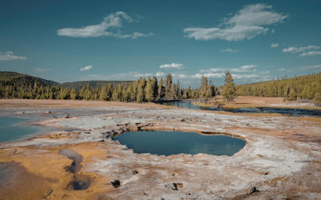 A natural hot spring surrounded by trees and mountains under a blue skyの写真素材