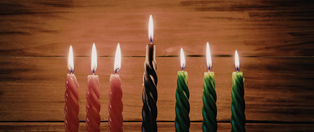 A row of lit candles in red, green, and black colors on a wooden background, symbolizing celebration and festivity.の写真素材