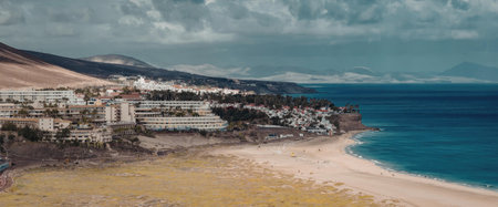 A picturesque coastal town situated on a cliffside overlooking a sandy beach and vast ocean waters...