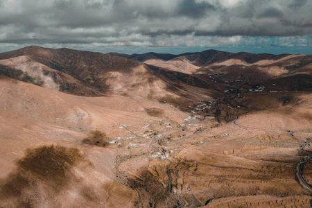An aerial view of a small town nestled in a valley surrounded by rolling hills and mountains under a...