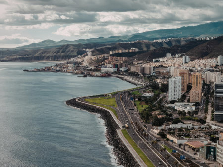 An aerial view of a coastal city with a road running along the waterfront, surrounded by mountains...