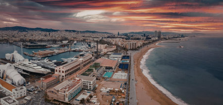 A panoramic view of a coastal city with buildings, pools, and a sandy beach leading to calm waters...