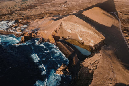 An aerial view of rugged coastal cliffs and ocean waves crashing against the shore, with a vast...