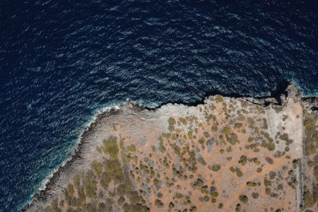 An aerial image of a rugged coastline with a mix of rocky shores, sparse vegetation, and clear blue...