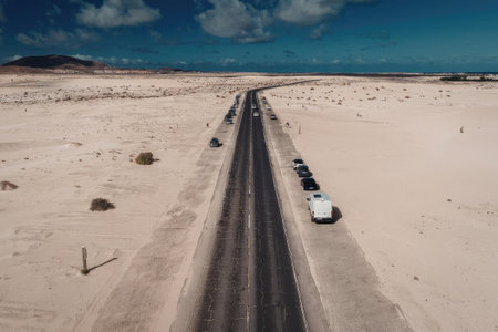 An aerial view of a long, straight road cutting through a vast desert landscape with a few vehicles...