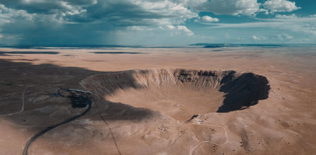 An aerial view of a vast desert landscape featuring a large crater with a vehicle nearby, showcasing the natural geological formation under a cloudy sky.の写真素材
