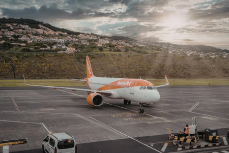 An airplane is parked on the tarmac at an airport with a city and mountains in the background.