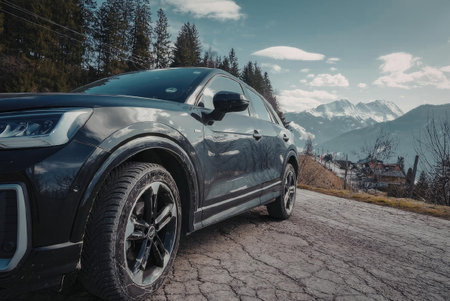 A dark gray SUV parked on a cracked road with mountains and trees in the background