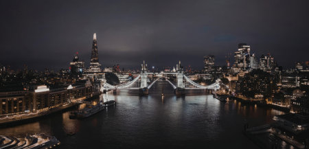 A nighttime view of a cityscape featuring Tower Bridge and the River Thames, with a dark and cloudy...