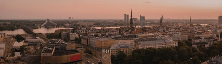 A panoramic view of a city during sunset, showcasing a mix of buildings and a river