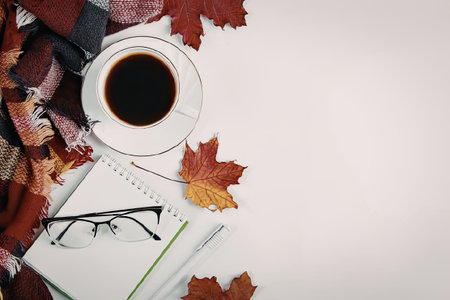 A serene autumnal setup featuring a cup of coffee, notebook, glasses, and vibrant fall leaves on a...