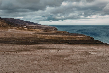 A scenic view of a rugged coastline with a cloudy sky, featuring a vast expanse of water and a dirt...