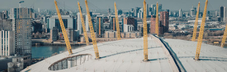 A construction site with multiple yellow cranes on a large concrete area, surrounded by city...