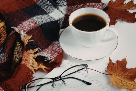 A warm and cozy still life arrangement featuring a cup of coffee, a plaid blanket, glasses, and...