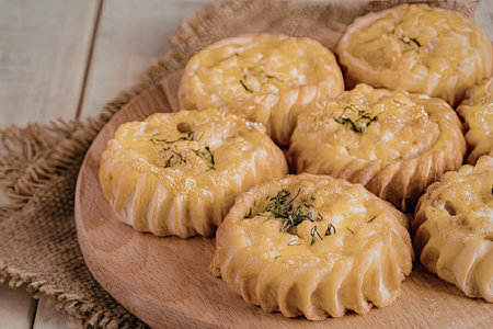 A wooden plate holds several golden brown pastries, topped with herbs and arranged on a rustic...