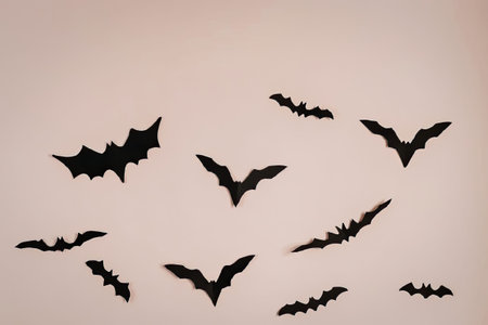 A group of black bats flying in different directions against a soft pink background, creating a...