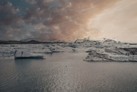 A serene landscape of icebergs floating in a body of water, with a cloudy sky and a glacier in the...