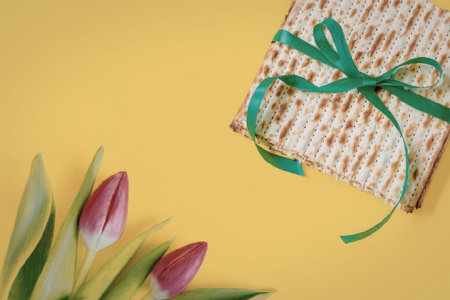 A gift wrapped in brown paper with a green ribbon and three pink tulips on a bright yellow...