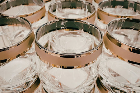 A close-up view of multiple glasses with gold rims filled with water, showcasing their reflective...