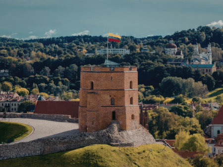 A tall brick tower with a flag on top stands on a grassy hill, overlooking a small town with trees...