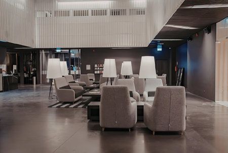 A modern lounge area with comfortable seating, featuring gray chairs and white lampshades, set against a backdrop of dark walls and polished floors.の写真素材