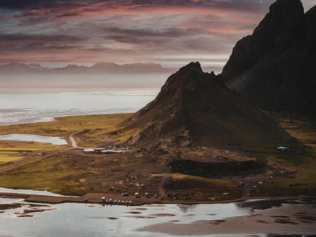 A serene mountain landscape at sunset with a body of water in the foreground and a vast sky with...