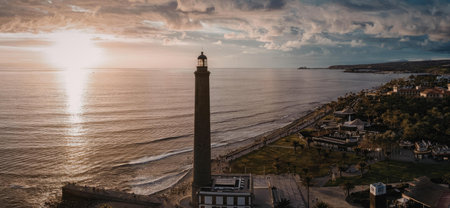 A serene lighthouse by the sea during sunset with a town nearbyの写真素材
