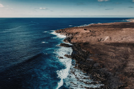A scenic view of ocean waves crashing against a rocky shoreline under a clear blue sky.