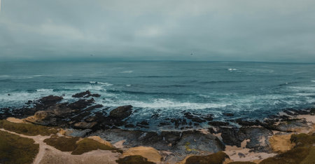 A scenic view of ocean waves crashing against a rocky shoreline on a cloudy day.
