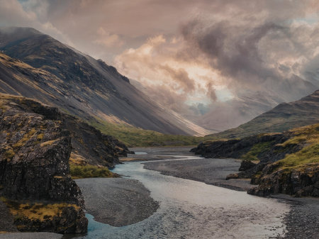 A serene river flows through a valley surrounded by mountains under a cloudy sky.