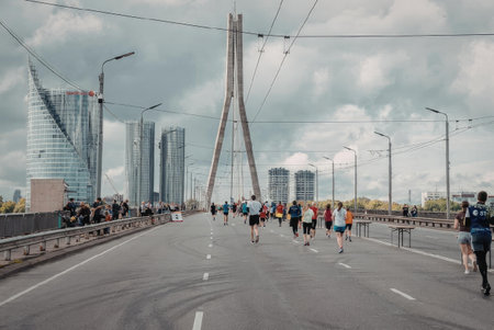 A group of people running on a city bridge with a modern architectural backgroundの写真素材